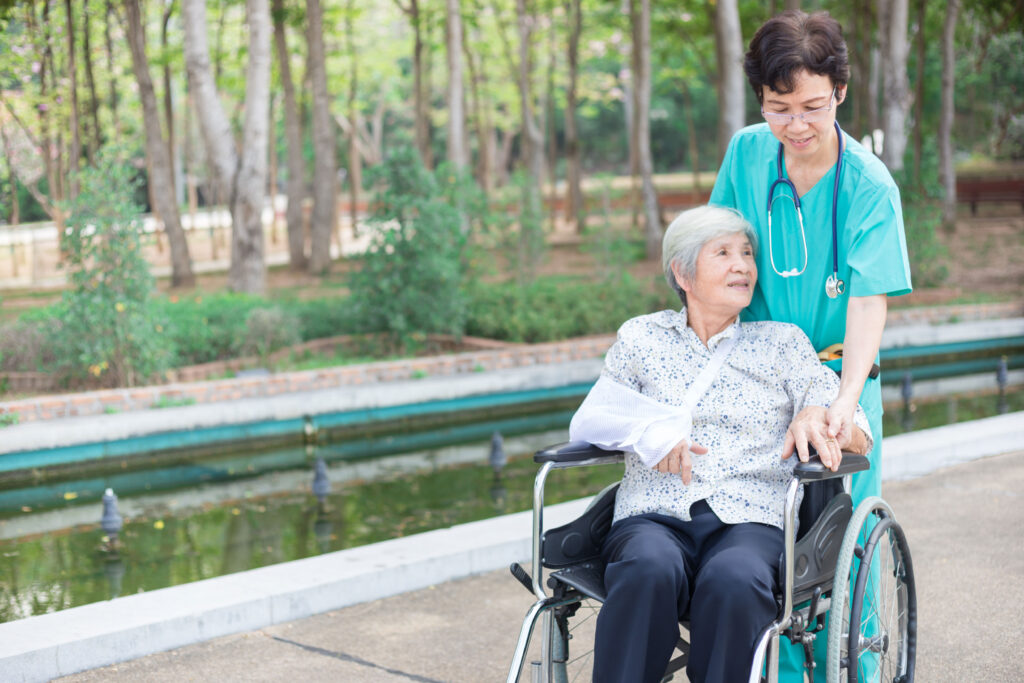 Nurse walking with an elderly patient seated in a wheelchair outdoors
