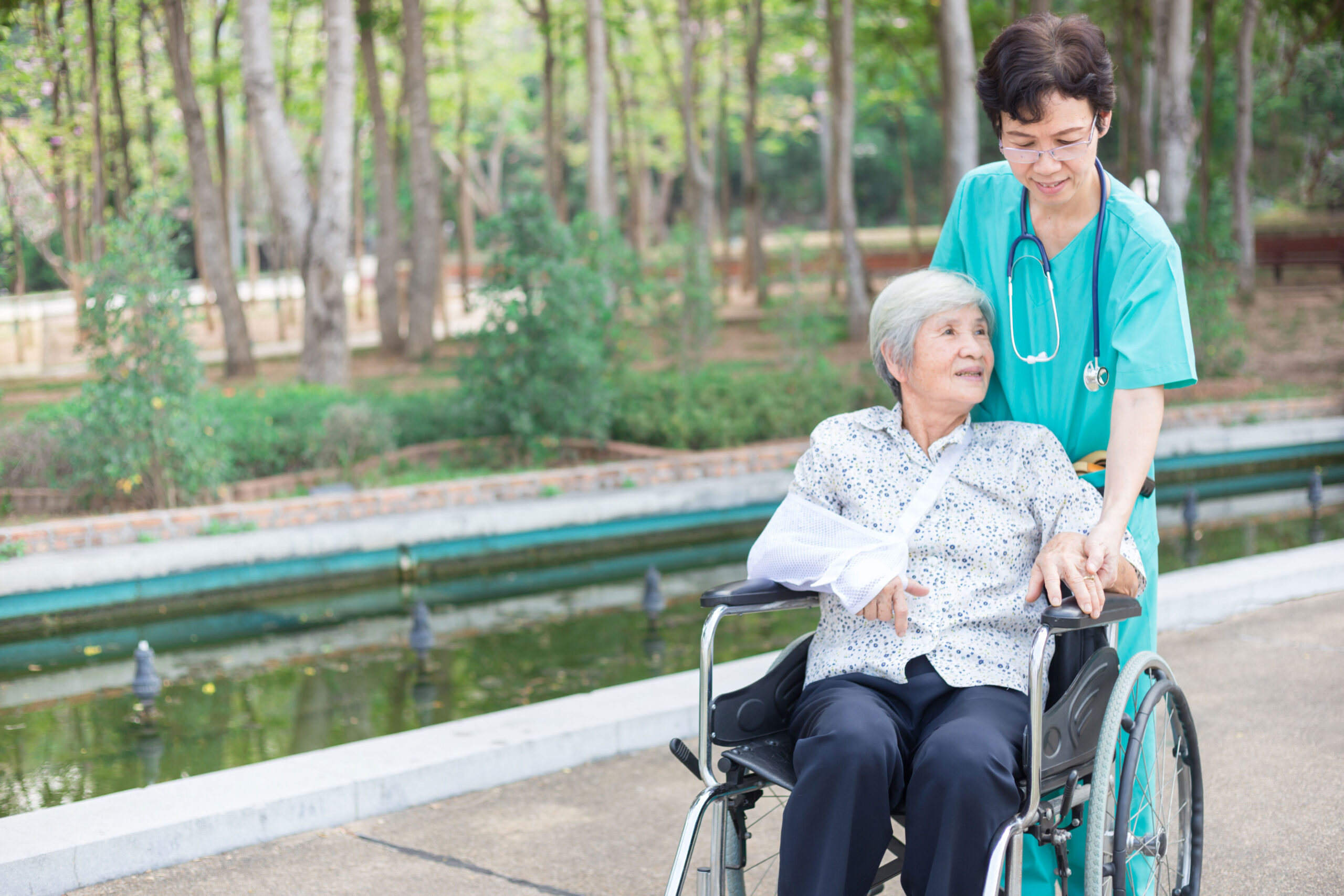 Nurse walking with an elderly patient seated in a wheelchair outdoors